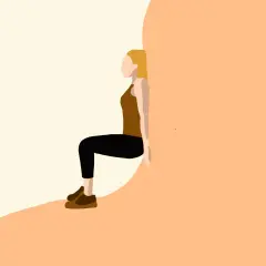 Kobieta w brązowym topie i czarnych legginsach wykonuje ćwiczenie wall sit, opierając plecy o ścianę.