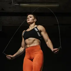 Silna kobieta w sportowym stroju wykonuje skakanie na skakance. Intensywny trening w mrocznym wnętrzu.