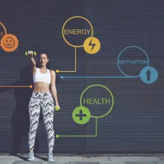 Kobieta ćwiczy z hantlami na tle ciemnej ściany z grafiką symbolizującą zdrowie, energię i motywację.