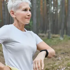 Kobieta z krótkimi siwymi włosami, ubrana w białą koszulkę, cieszy się treningiem cardio w lesie.