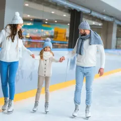 Rodzina na lodowisku, trzymająca się za ręce podczas jazdy na łyżwach.