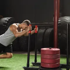 Mężczyzna wykonuje ćwiczenie sled push, pchając obciążony sprzęt. Trener obserwuje jego wysiłek.