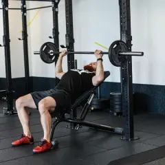 Mężczyzna z brodą wykonuje ćwiczenie incline press na ławce skośnej w siłowni.