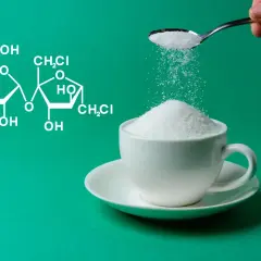 Struktura chemiczna sukralozy obok filiżanki białego proszku, który jest dosypywany z łyżeczki.
