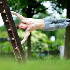 Mężczyzna wykonuje figurę "human flag" na drabinie. To przykład tego, kalistenika co to za dyscyplina – siła i kontrola ciała.