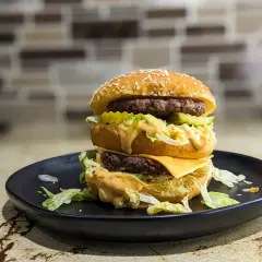 Podwójny burger z serem, sałatą i sosem na czarnym talerzu. Zastanawiasz się, ile kalorii ma Big Mac?