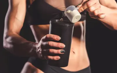 Kobieta dodaje proszek do shakera. Idealny shake proteinowy przepis na regenerację po treningu.