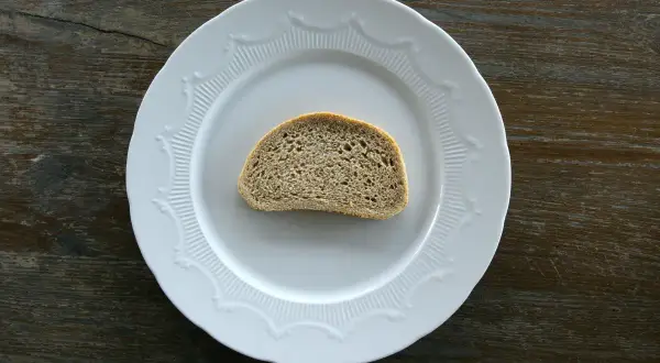 Jedna kromka chleba na białym talerzu. Zastanawiasz się, ile kromka chleba kcal ma?