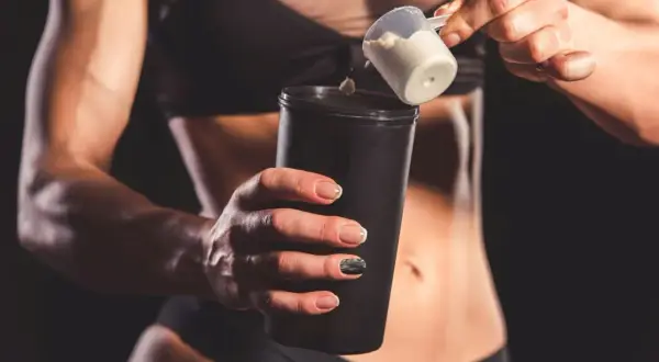 Kobieta dodaje proszek do shakera. Idealny shake proteinowy przepis na regenerację po treningu.