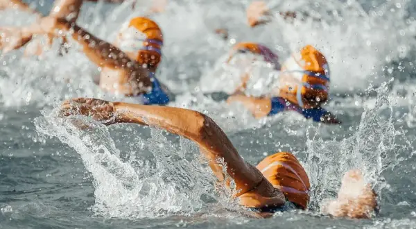 Pływacy w czepkach ścigają się w wodzie. Intensywny wysiłek podczas tego multisport classic.