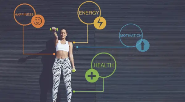 Kobieta ćwiczy z hantlami na tle ciemnej ściany z grafiką symbolizującą zdrowie, energię i motywację.