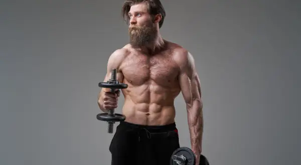 Mężczyzna z imponującą brodą wykonuje ćwiczenia na biceps, trzymając hantle do hammer curls.
