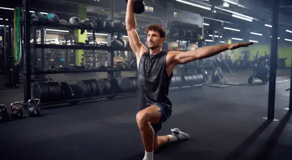 Mężczyzna w siłowni wykonuje ćwiczenie z kettlebell. To tbc co to za ćwiczenie, ale wygląda na skuteczne.