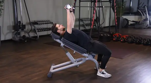 Mężczyzna wykonuje ćwiczenie incline dumbbell press na ławce skośnej, podnosząc ciężarki nad klatkę piersiową.