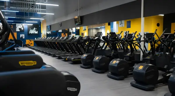 Rzędy bieżni i orbitreków w siłowni Just Gym. Dowiedz się, jak wejść na Multisport i zacząć trening.