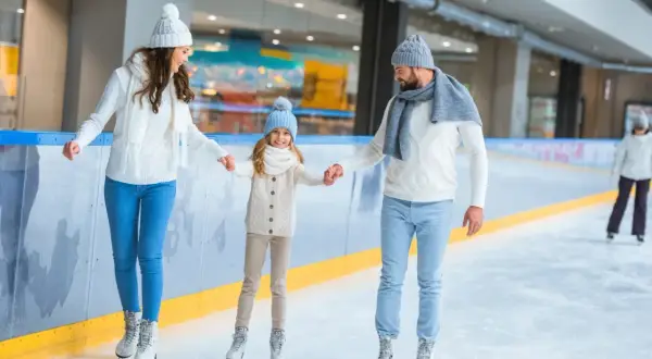 Rodzina na lodowisku, trzymająca się za ręce podczas jazdy na łyżwach.