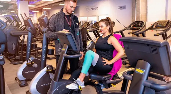 Trener pomaga kobiecie na rowerku stacjonarnym. Czy MCFit honoruje Multisport? Sprawdź, zanim zaczniesz trening!