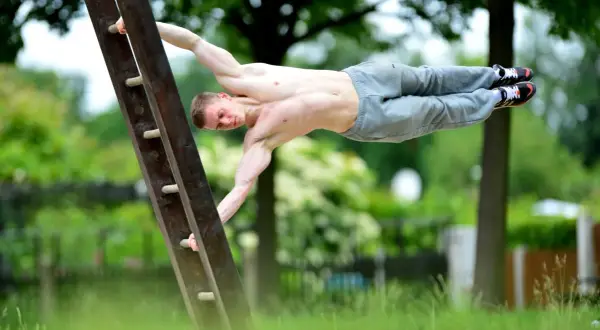 Mężczyzna wykonuje figurę "human flag" na drabinie. To przykład tego, kalistenika co to za dyscyplina – siła i kontrola ciała.
