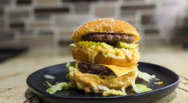 Podwójny burger z serem, sałatą i sosem na czarnym talerzu. Zastanawiasz się, ile kalorii ma Big Mac?