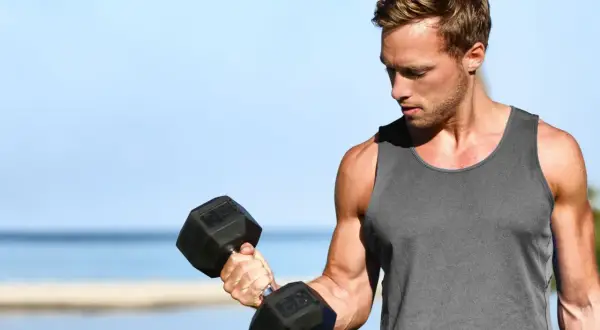 Mężczyzna ćwiczy biceps na plaży, zastanawiając się, ile serii na biceps w tygodniu da najlepsze efekty.