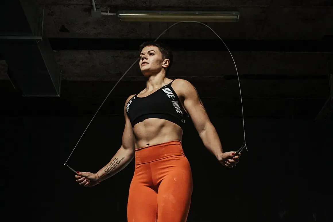 Silna kobieta w sportowym stroju wykonuje skakanie na skakance. Intensywny trening w mrocznym wnętrzu.