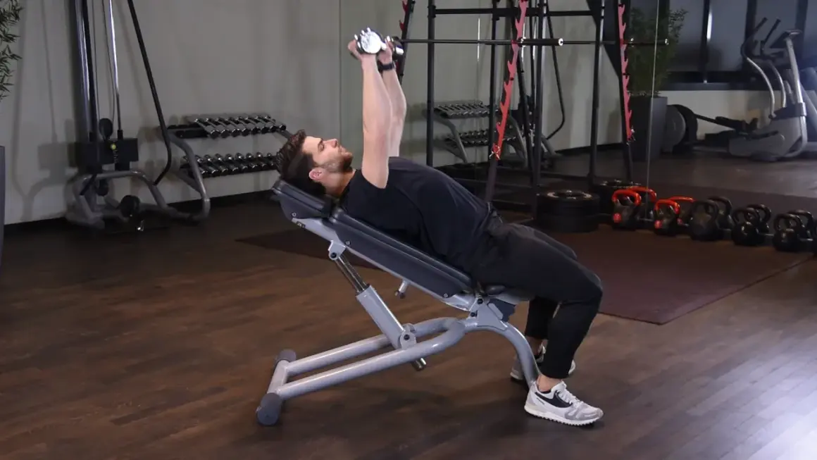 Mężczyzna wykonuje ćwiczenie incline dumbbell press na ławce skośnej, podnosząc ciężarki nad klatkę piersiową.