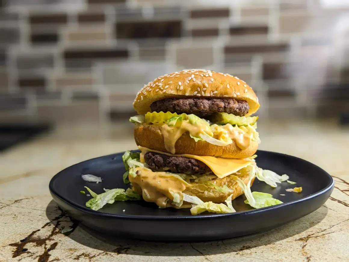 Podwójny burger z serem, sałatą i sosem na czarnym talerzu. Zastanawiasz się, ile kalorii ma Big Mac?
