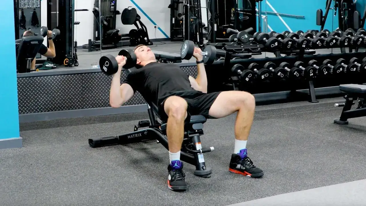 Mężczyzna wykonuje ćwiczenie incline dumbbell press na ławce skośnej, podnosząc ciężarki.