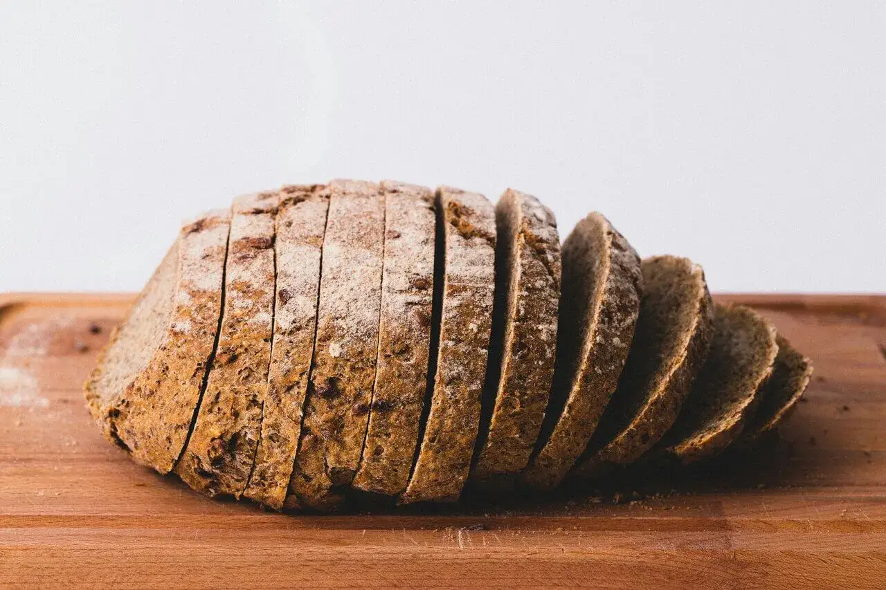 Pokrojona kromka chleba żytniego, posypana mąką, na drewnianej desce. Idealna na zdrowe śniadanie, z niską zawartością kcal.